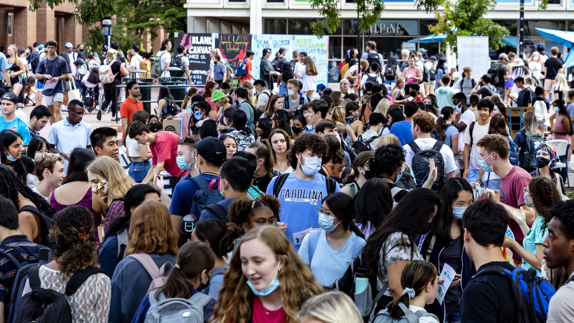 UNC campus scene. Students meet in front of the bookstore in large groups. Multiple are seen wearing masks.
