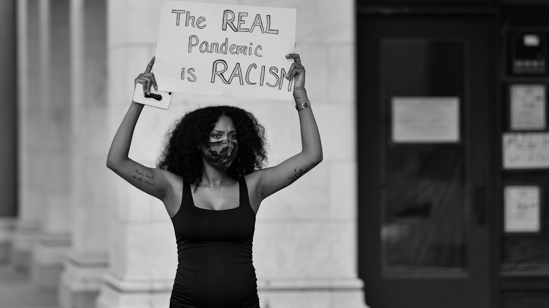a woman holds a sign that reads "the real pandemic is racism."