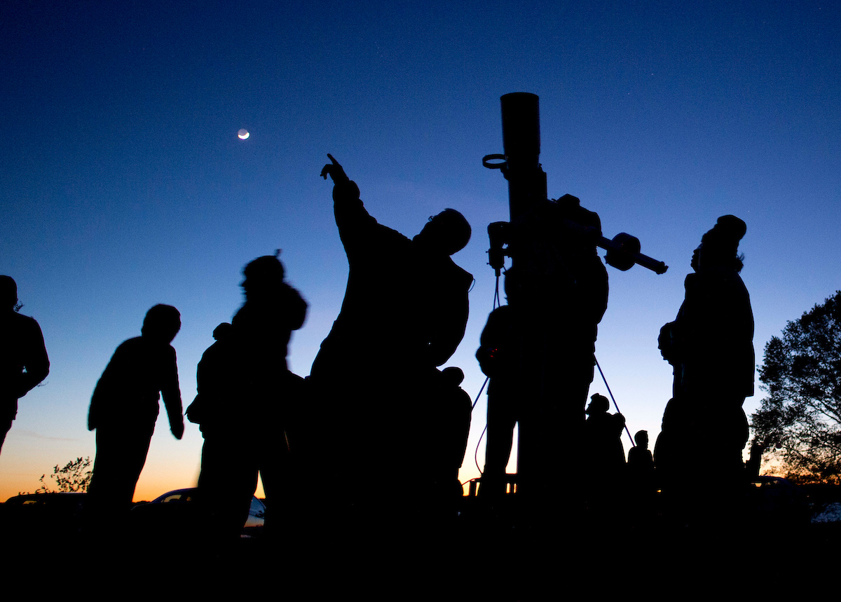 Silhouettes of people looking and pointing at the sky as it gets darker.