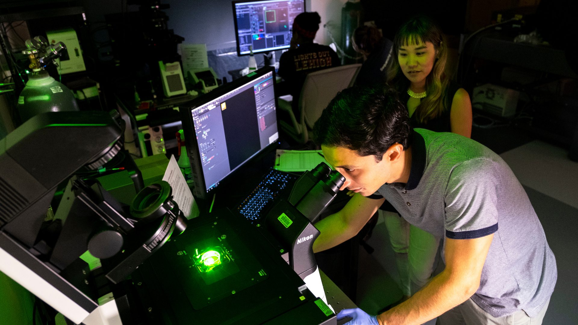 Researchers look through microscopes at a large computer setup.