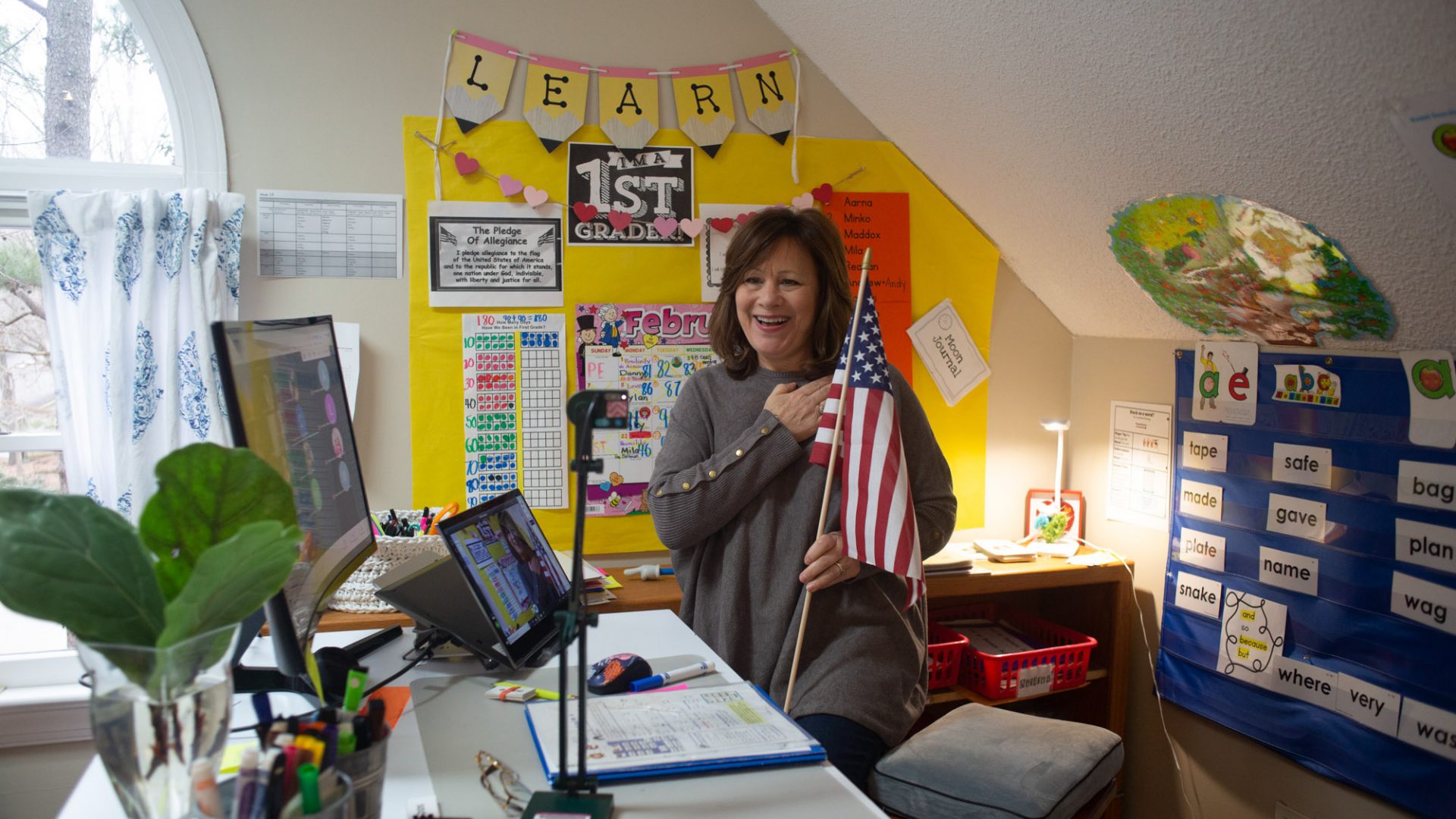 Woman holds an American flag as she puts her hand over her heart and conducts "The Pledge of Allegiance" over web-cam.