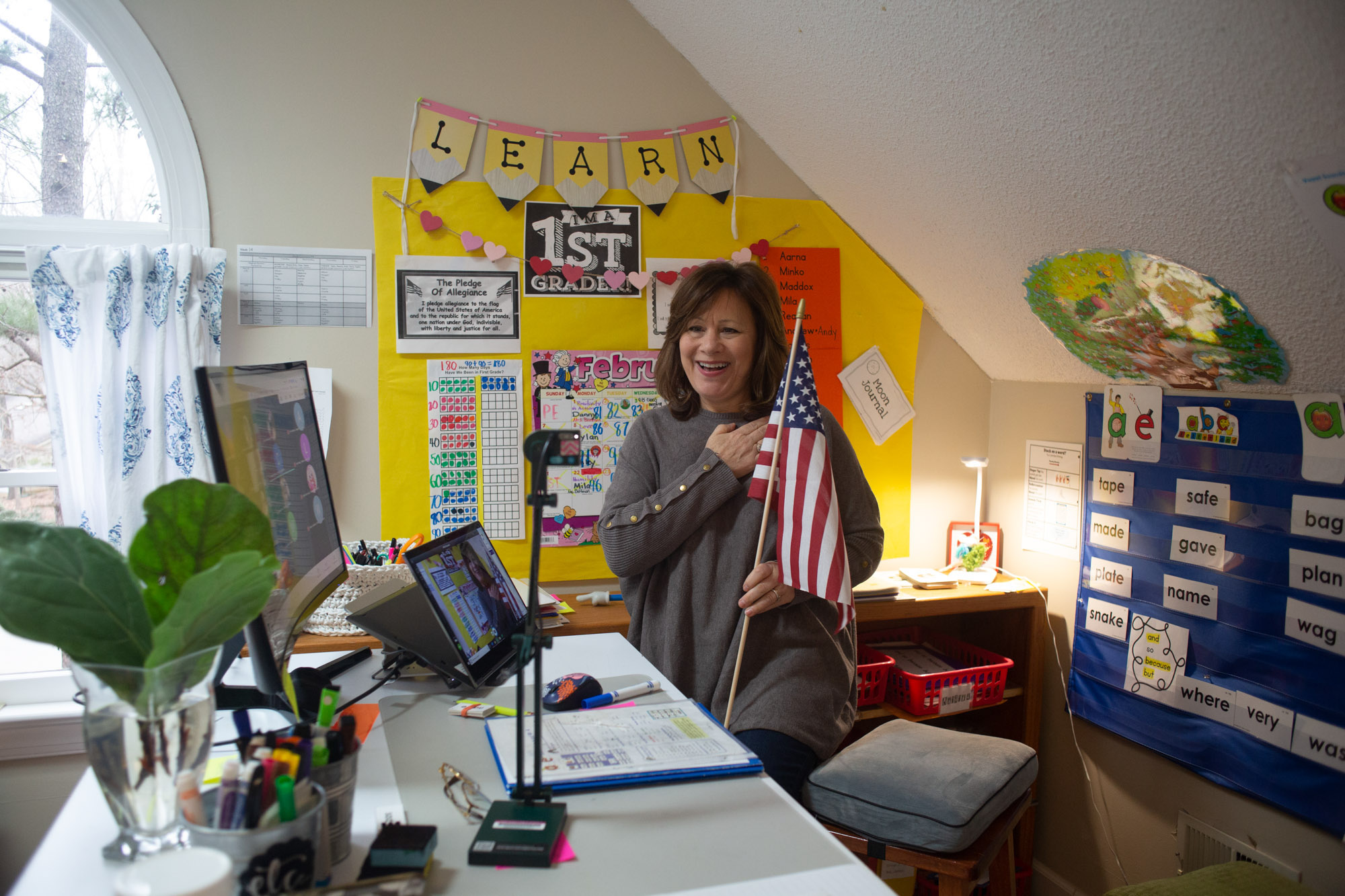 Woman holds an American flag as she puts her hand over her heart and conducts "The Pledge of Allegiance" over web-cam.