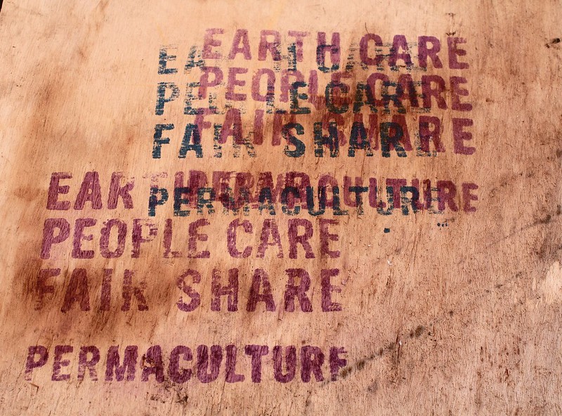 Photo of graffiti on the wall. Graffiti reads "Earth Care, People Care, and Fair Share" over and over again.
