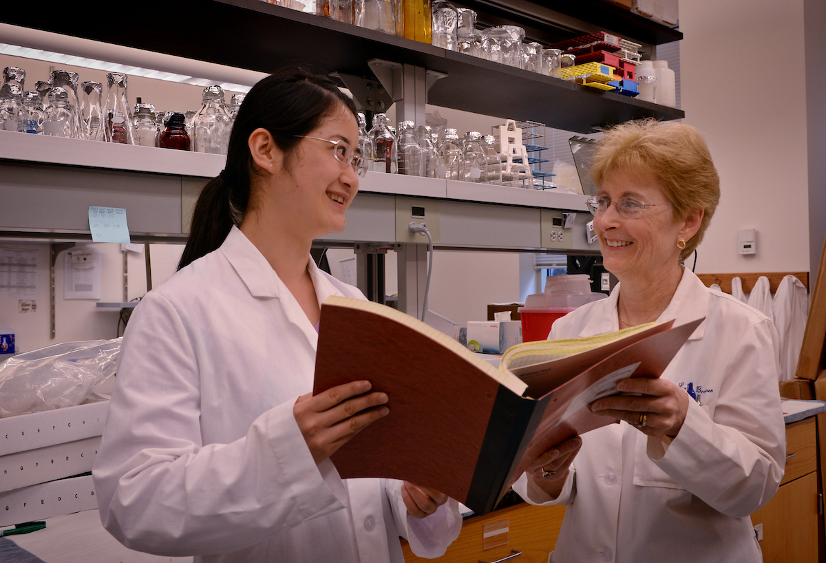 A UNC Pharmacy professor chats with a graduate student while looking over one of their books in a UNC Pharmacy lab.