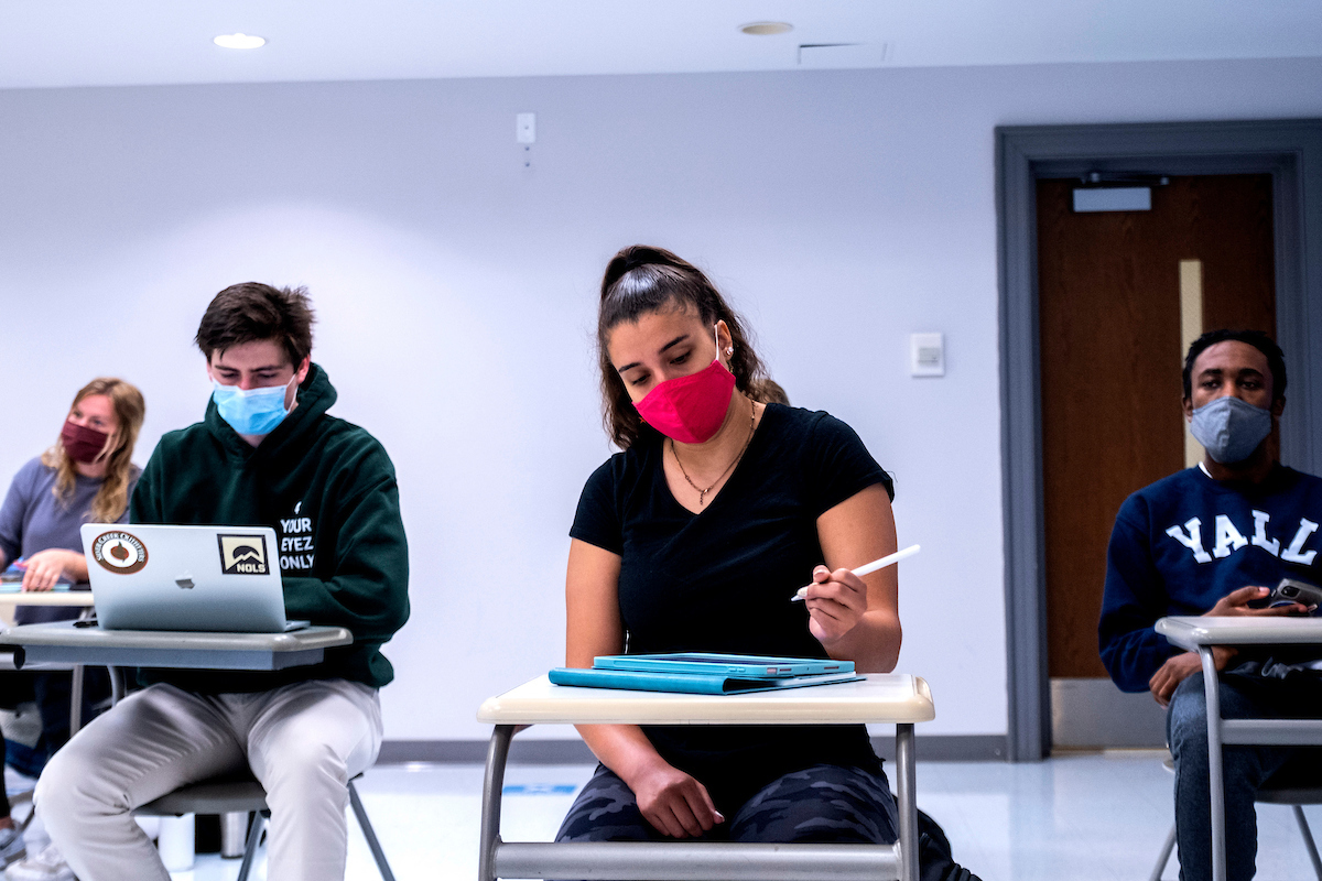 College students sit in a classroom, wearing their masks.