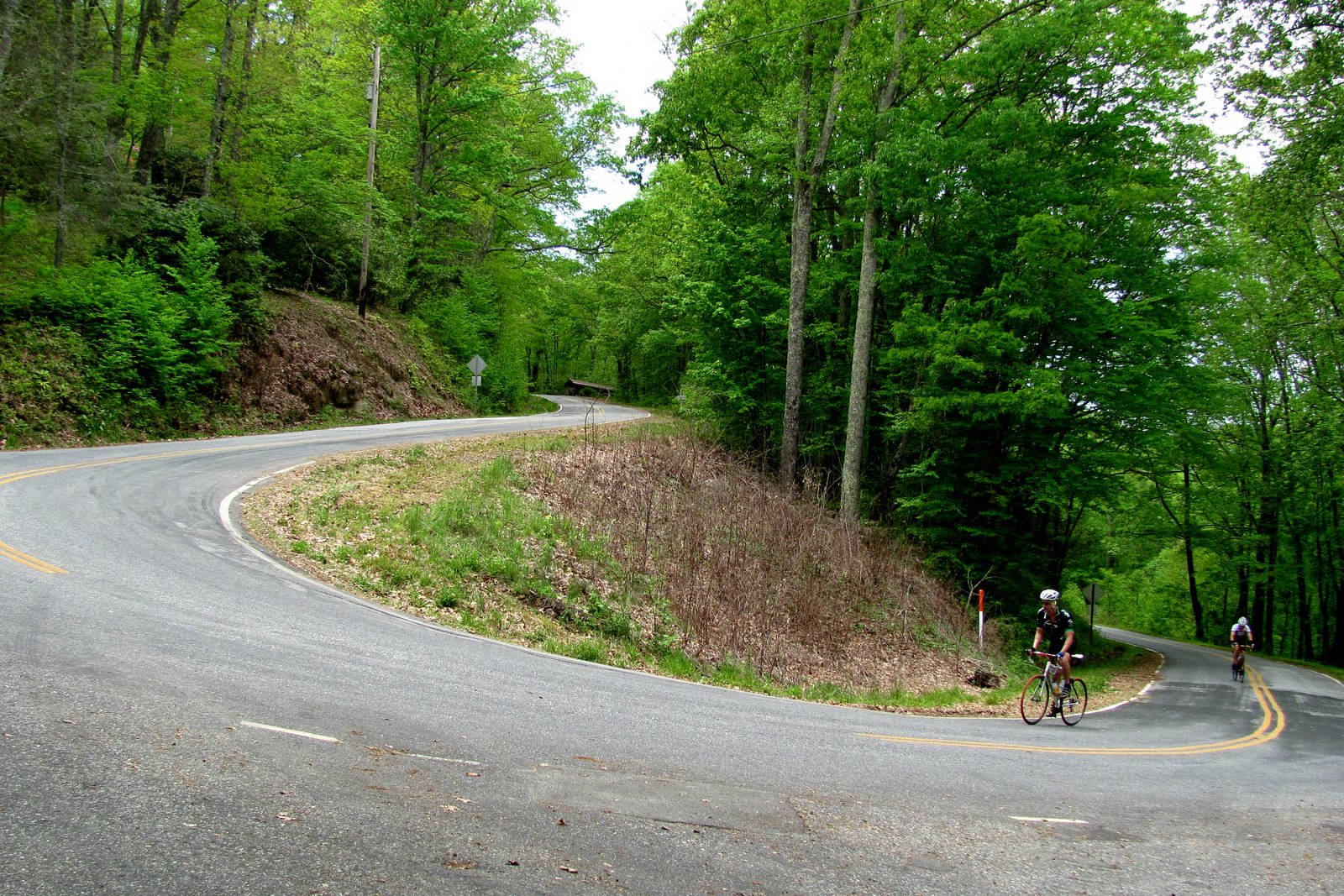 Image of a switch back road in the mountains of North Carolina with two bikers biking up the road.
