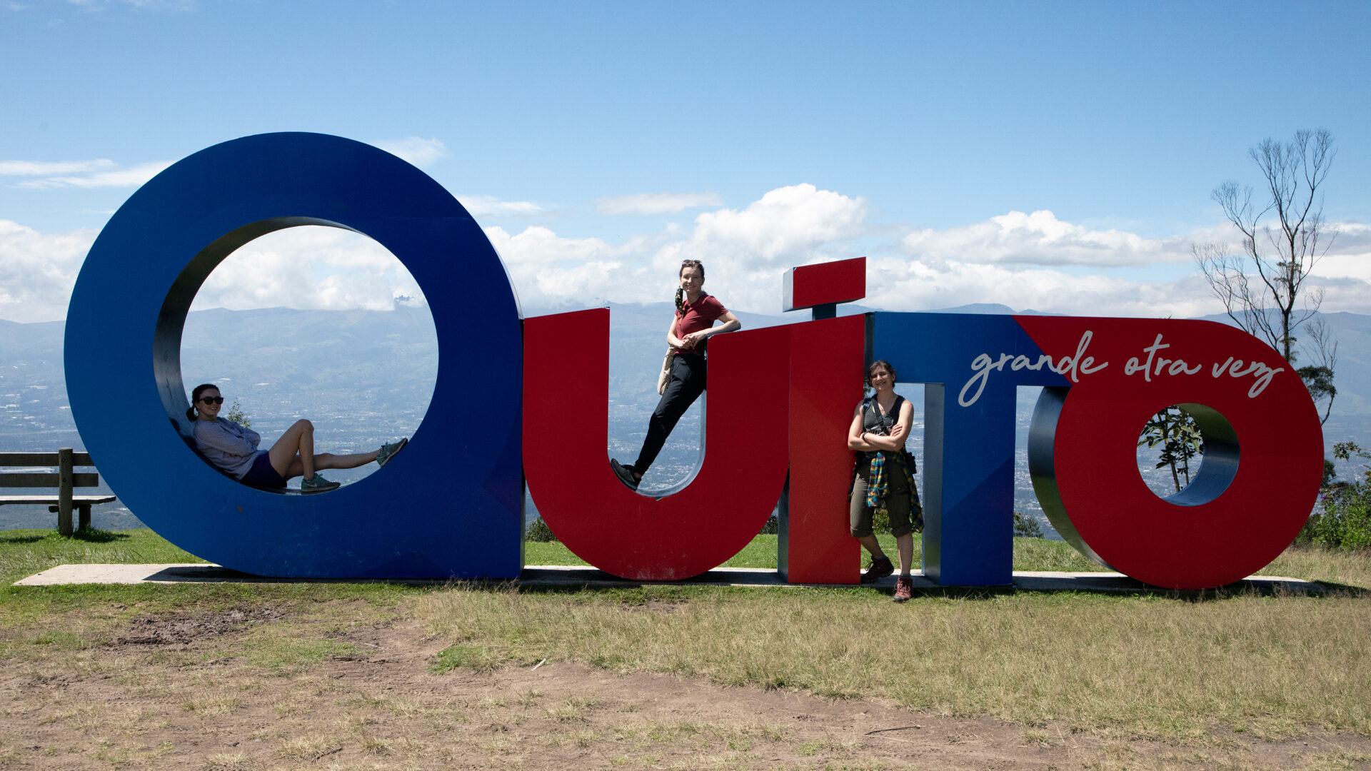 Three UNC research students sit in front of a large sign that says "Quito."