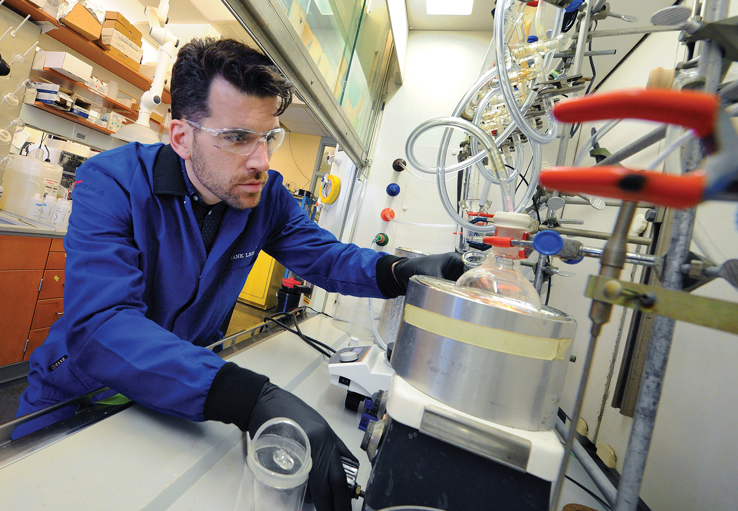 Photo of Frank Leibfarth in the lab wearing protective gear, bent over lab equipment.