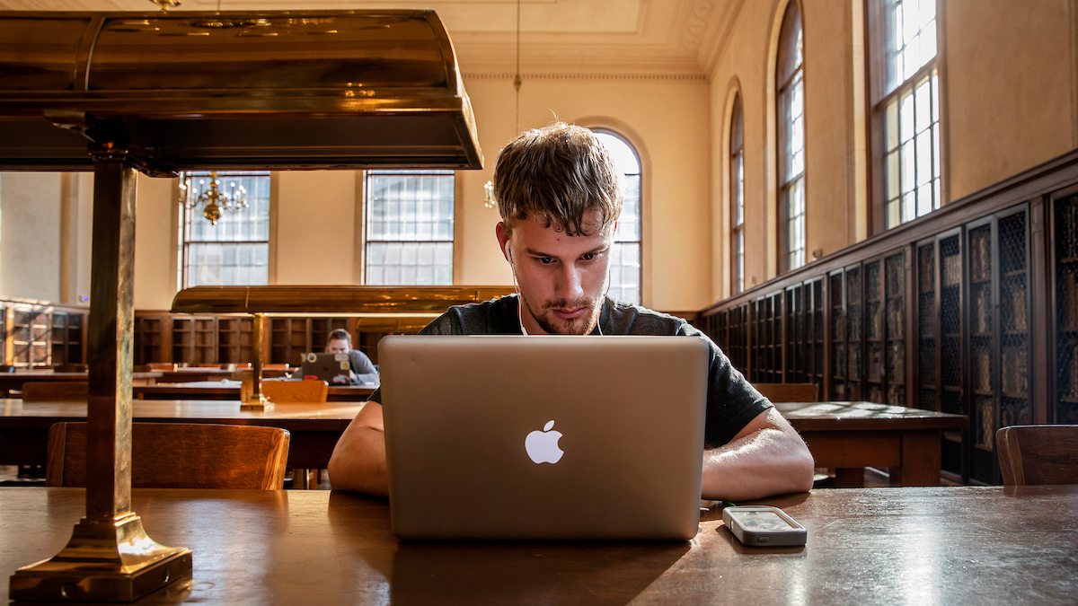 A student sits on their laptop in the Wilson Library reading room.
