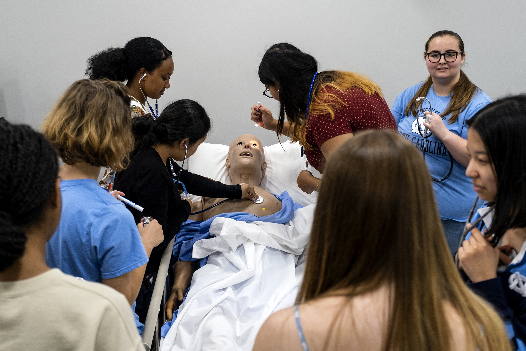 Nursing students crowd around a practice dummy on a stretcher.
