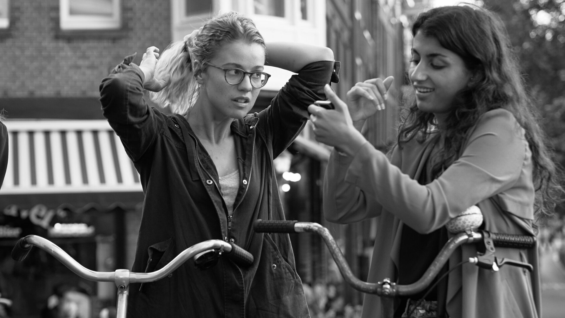 Two women stand with their bikes, one is signing and the other is putting up her hair.