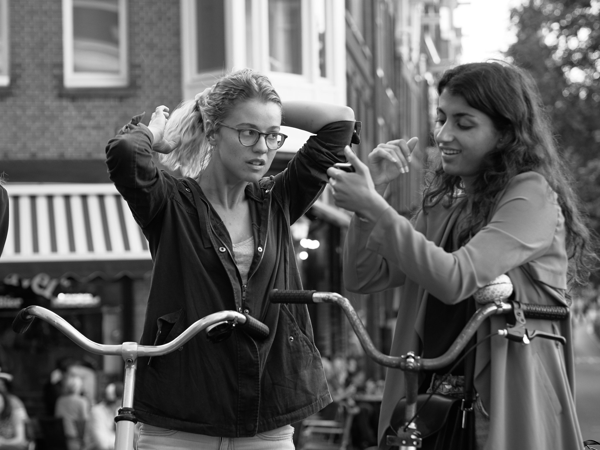 Two women stand with their bikes, one is signing and the other is putting up her hair.