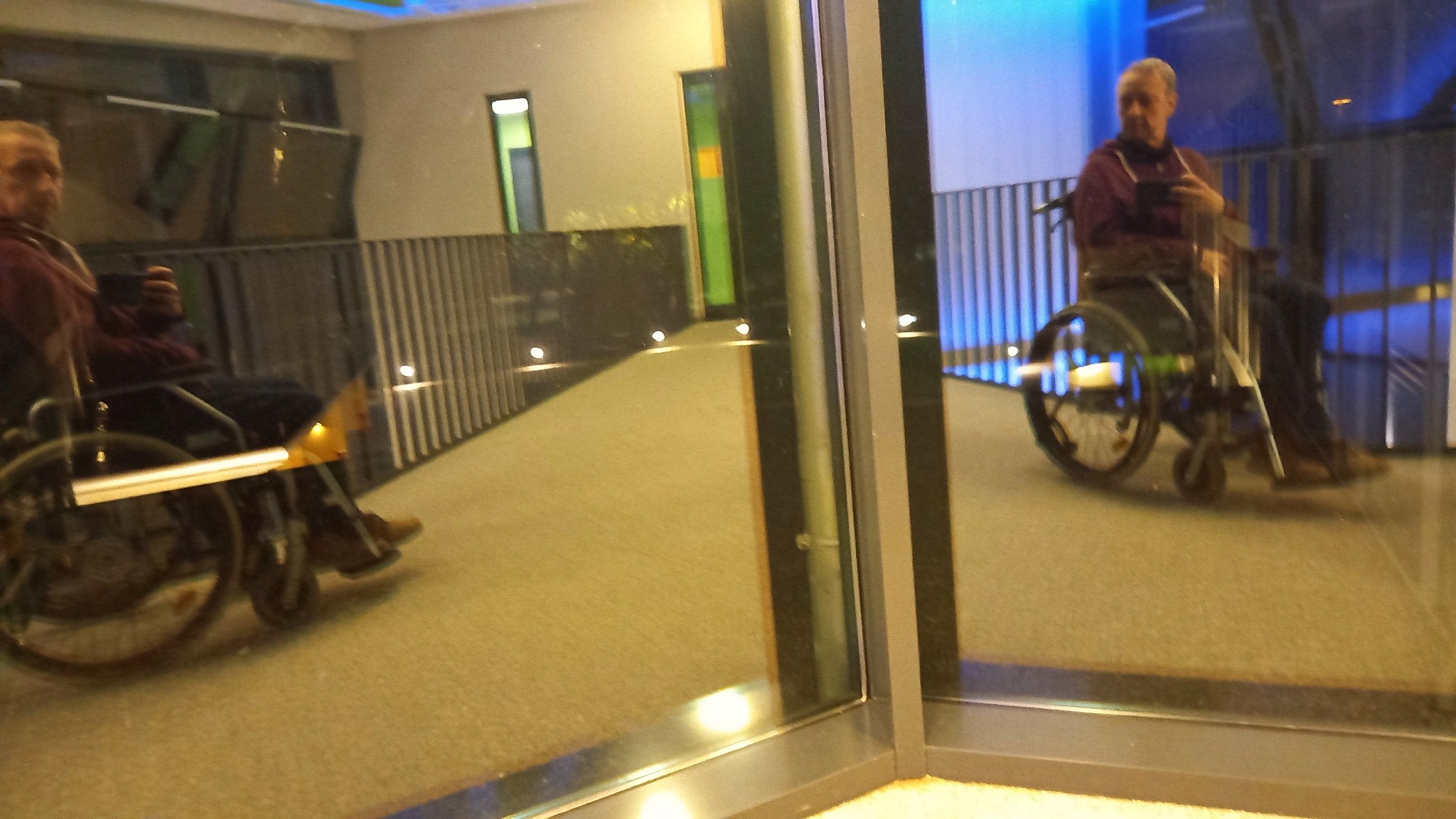 Photo of an older man's reflection as he sits in a wheelchair.