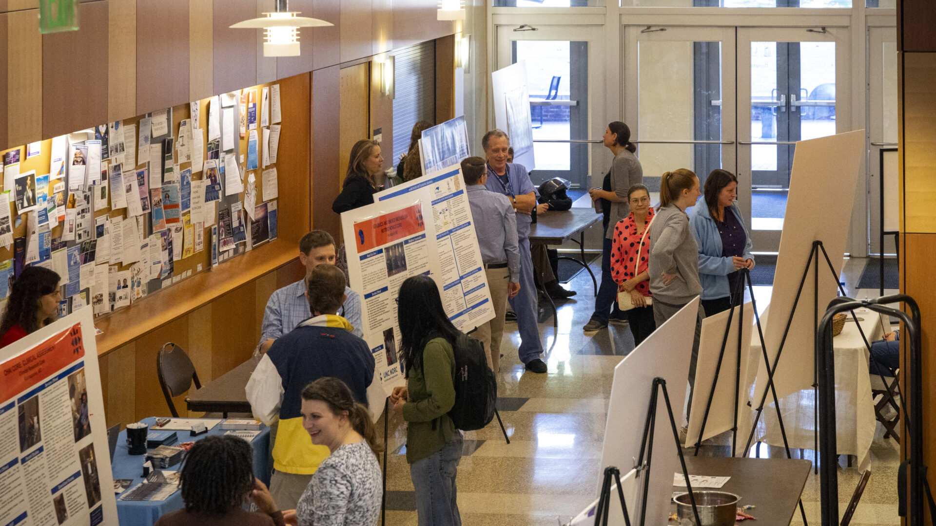 Researchers stand in a hall with their poster presentations on easels. People stop to chat about their research.