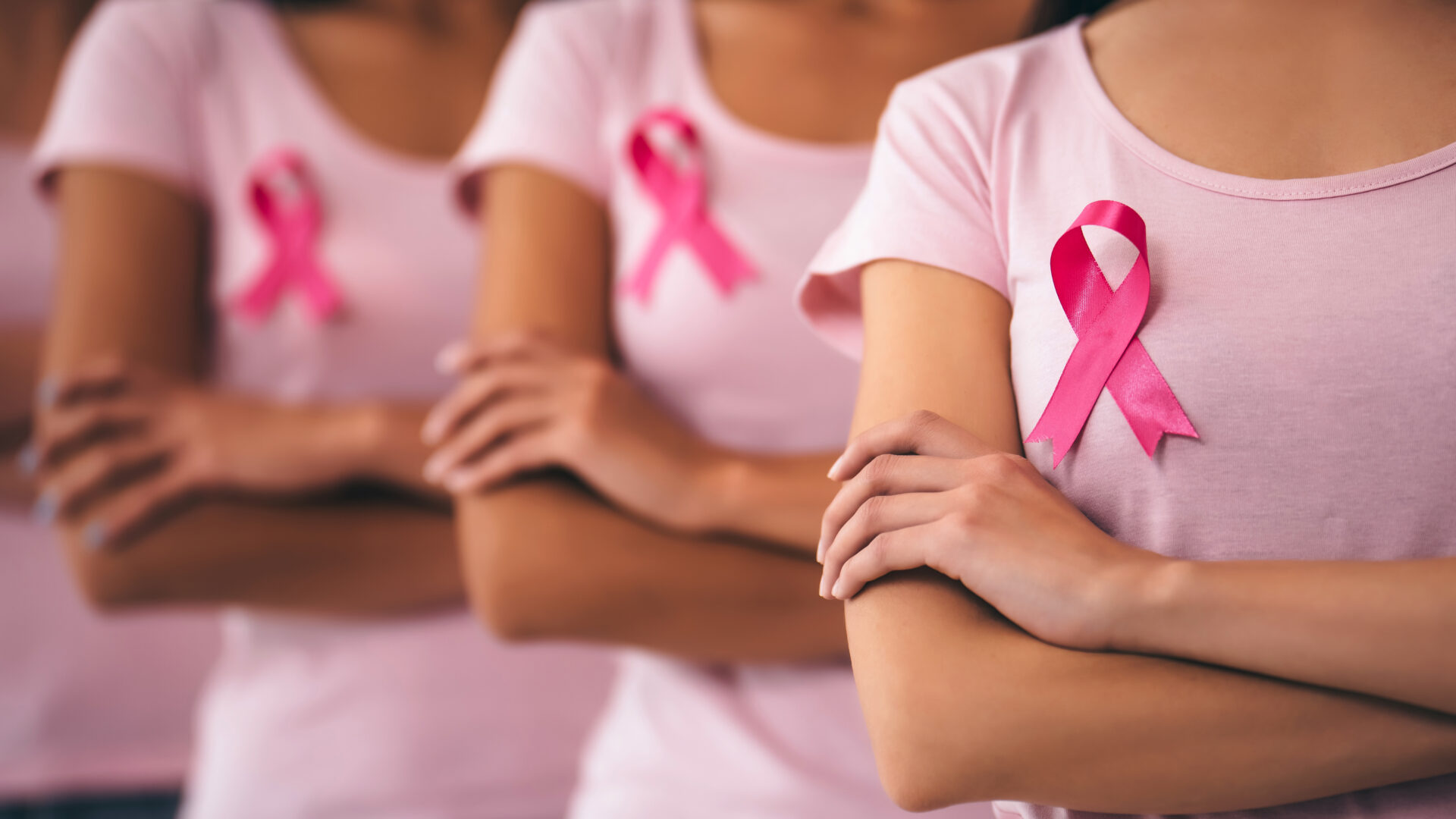 Group of women with pink ribbons pinned to their shirts and their arms crossed.