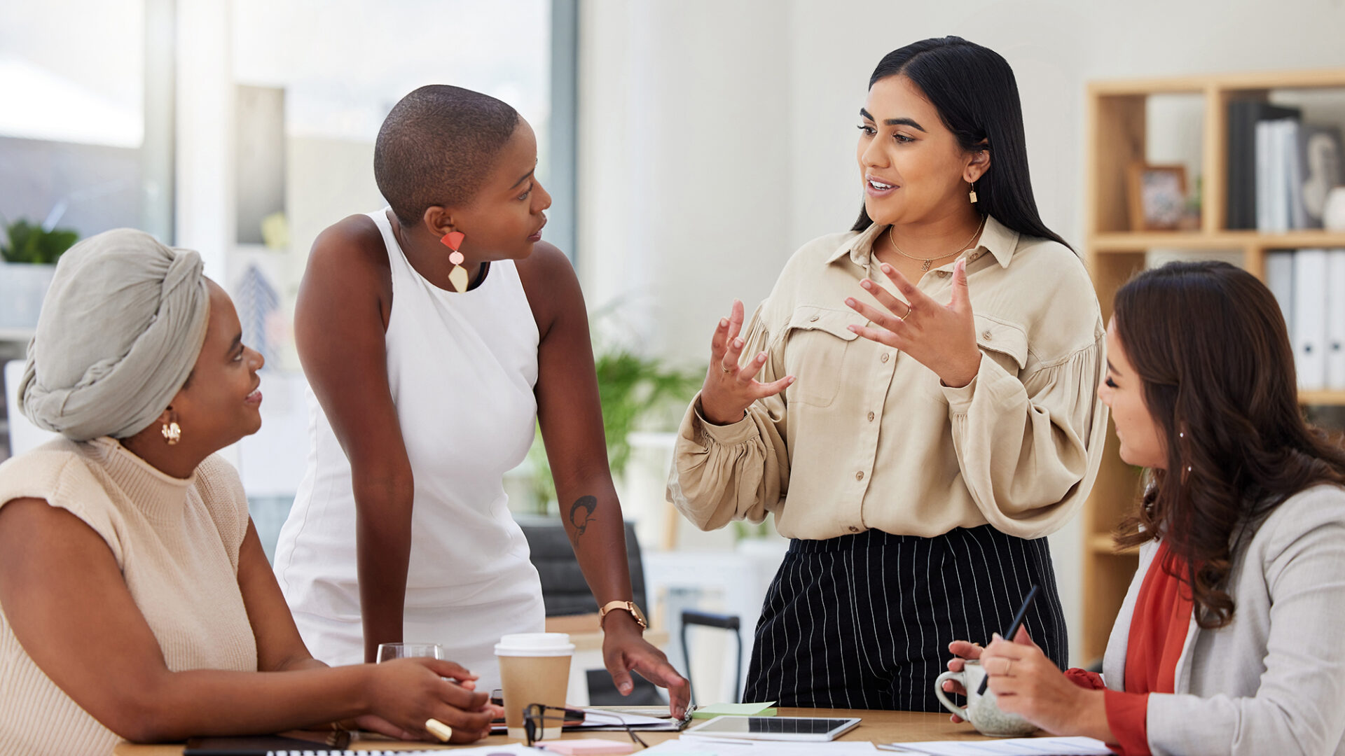 Women gather around a table, discussing.