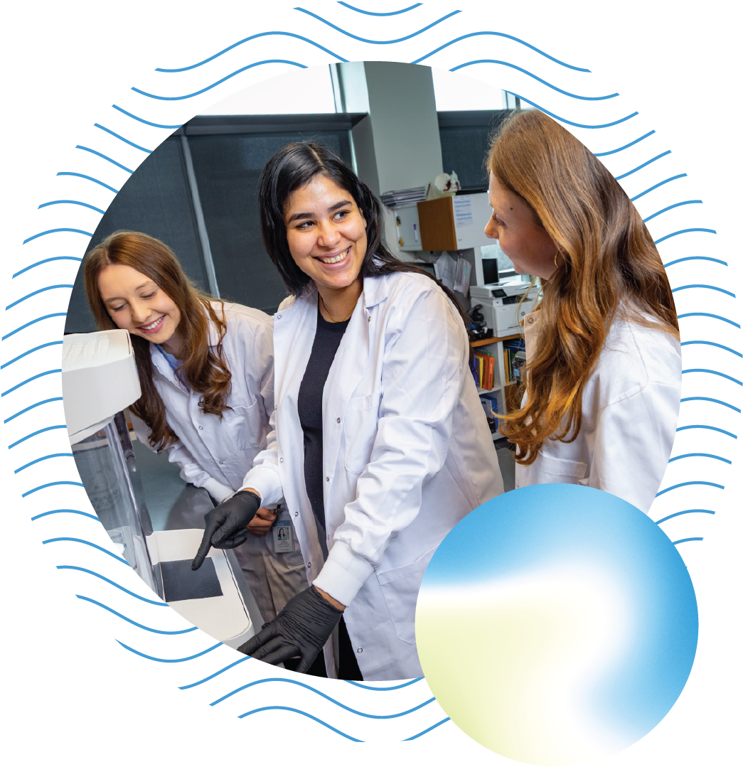 Three researchers smile at one another as they point to something on equipment in the lab.