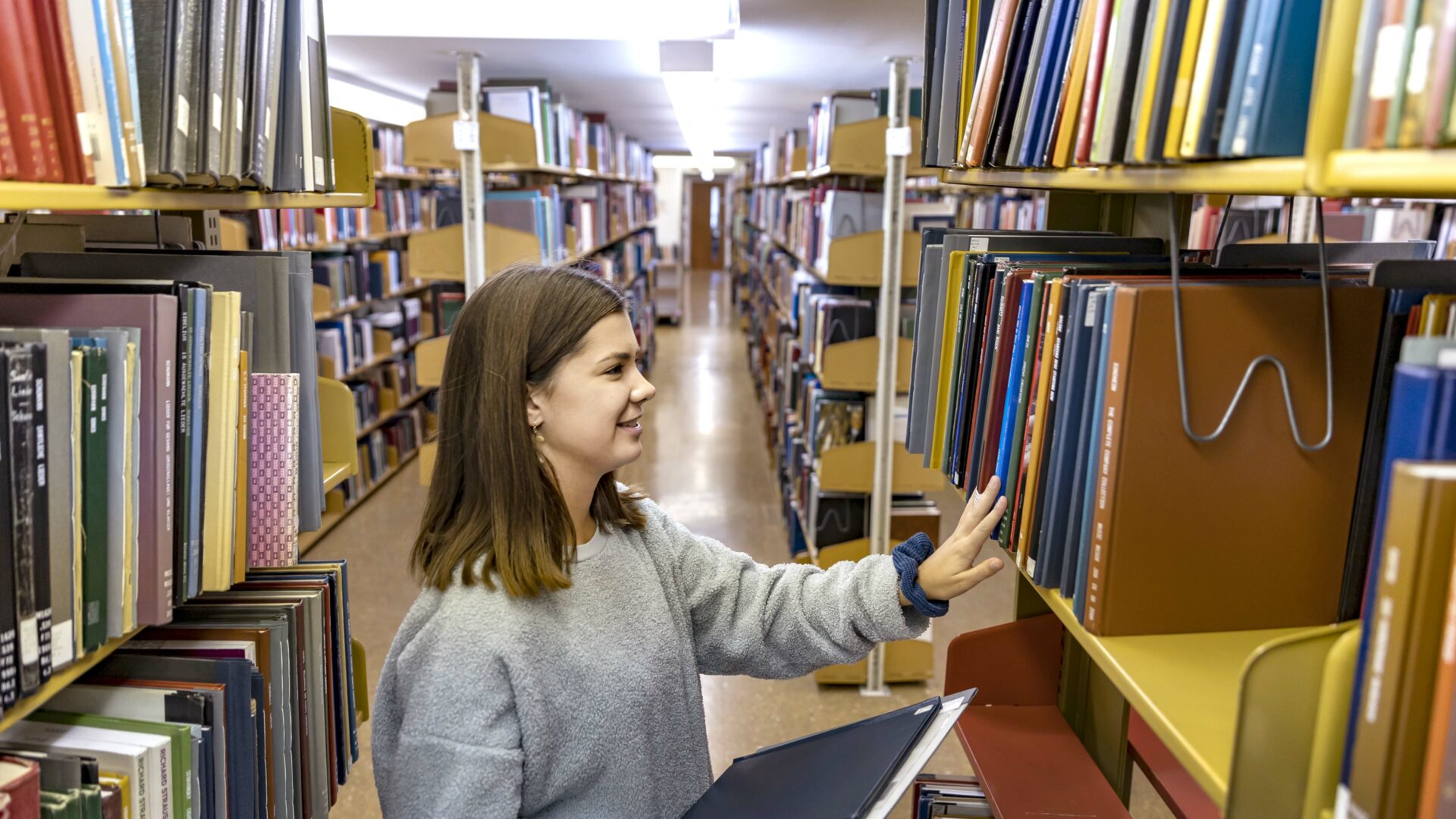 Girl placing a book into a bookshelf in a library