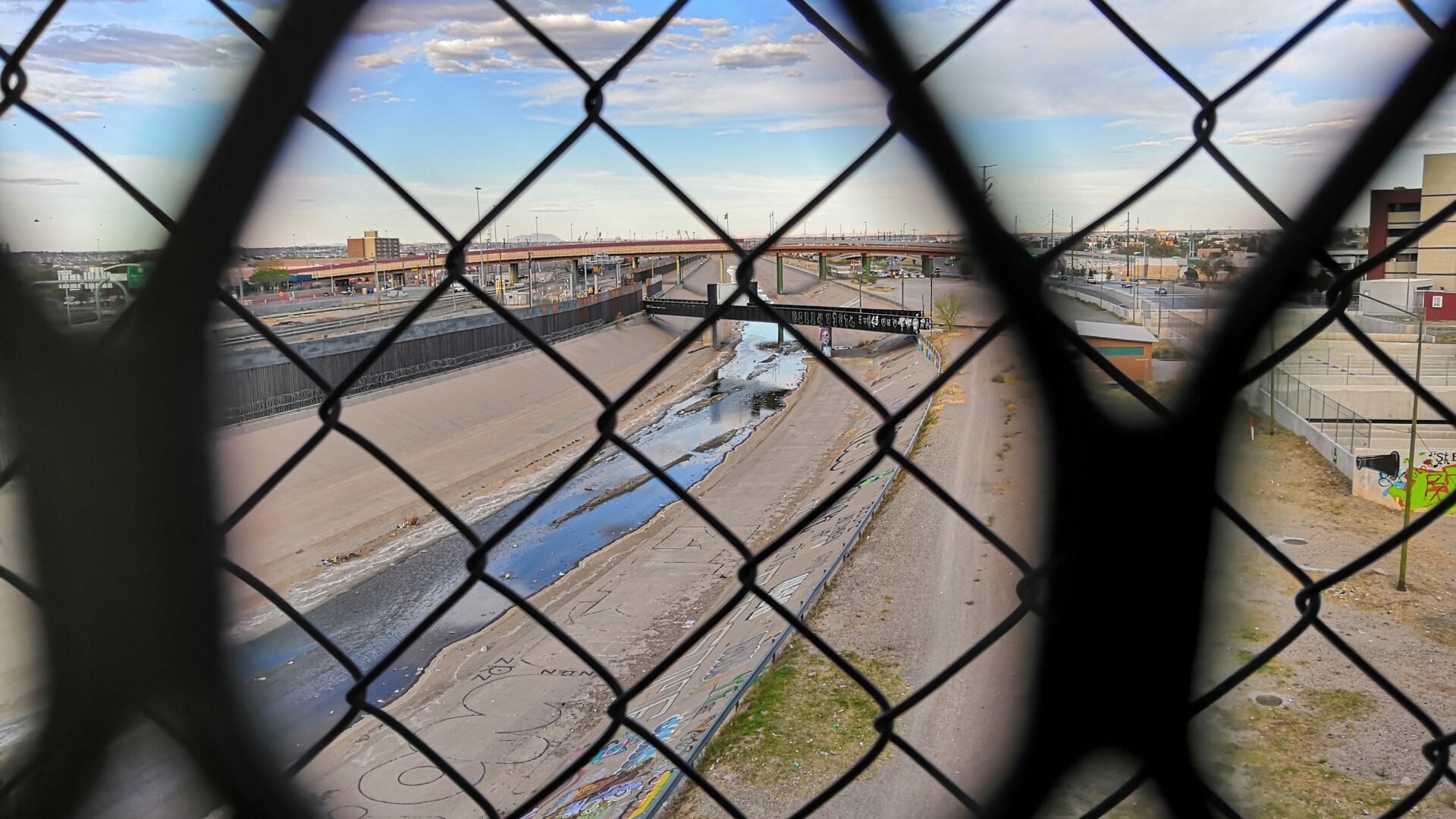 Photo taken through a chain link fence, looking over at a Mexican city from the U.S. border.