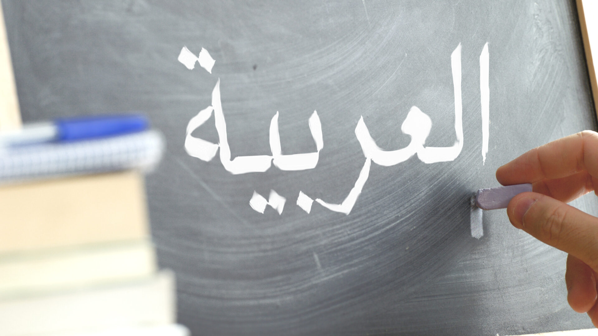 Someone writes an Arabic word on a chalk board.